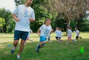 A group of kids running with an instructor during outdoor sports activities on a sunny day in a park.